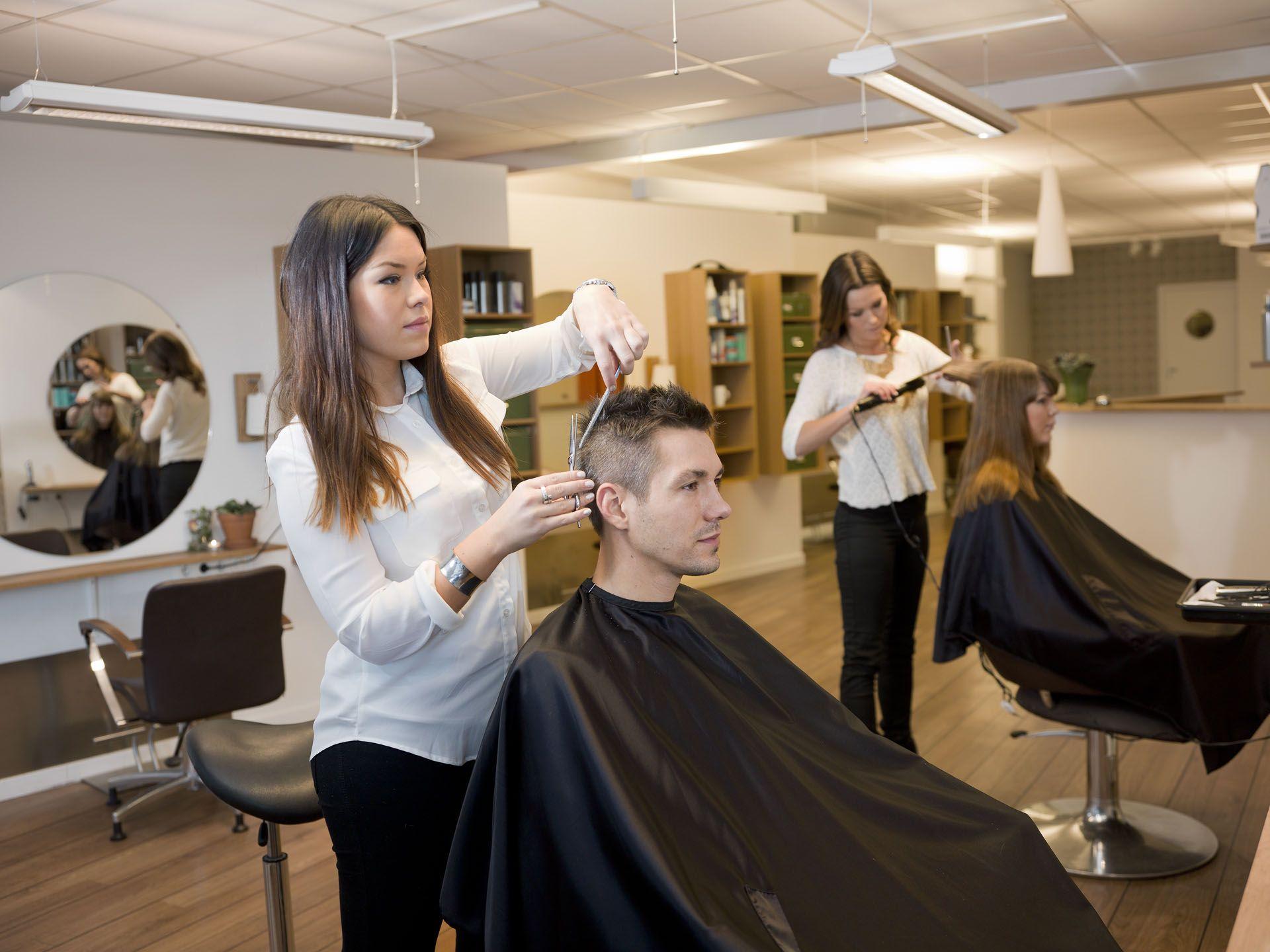 Une coiffeuse entrain de réaliser une coupe de cheveux sur un homme